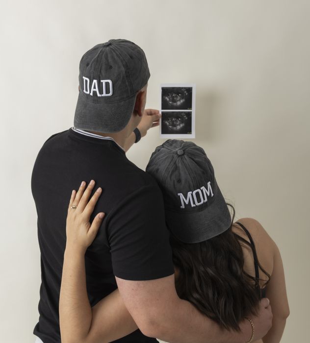 Pareja de espaldas con gorras DAD y MOM mostrando la ecografía