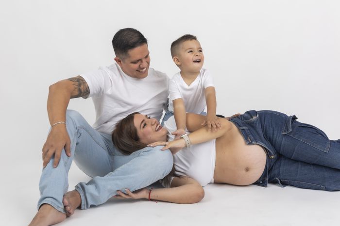 Mamá embarazada recostada en el piso riendo con su esposo y su hijo